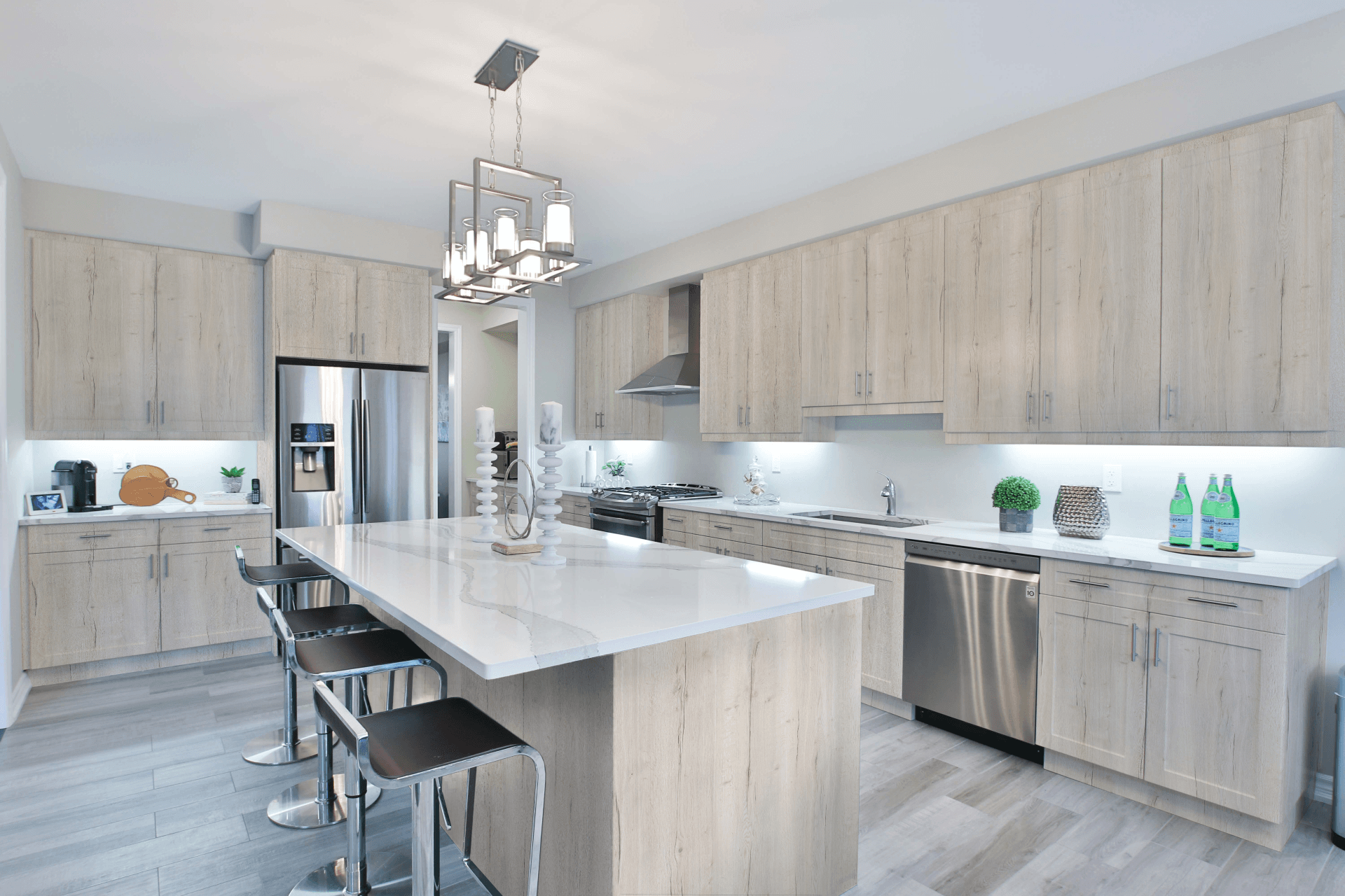 Modern kitchen with light wood cabinets, large island with white countertop, stainless steel appliances, and four stools. Bright, clean, and spacious.
