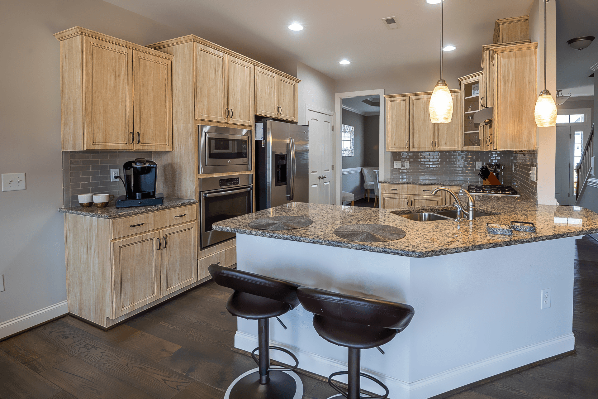 Modern kitchen with wooden cabinets, granite countertops, stainless steel appliances, and two pendant lights above an island with two brown stools.