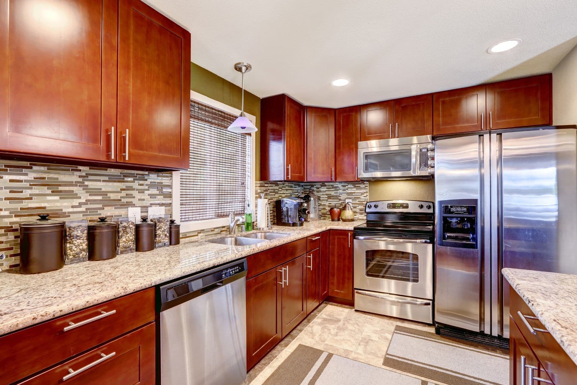 Modern kitchen with cherry wood cabinets, stainless steel appliances, granite countertops, and mosaic tile backsplash. Warm lighting creates a cozy feel.