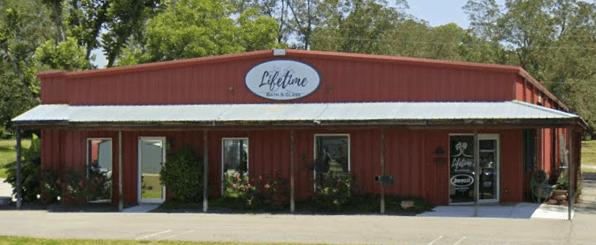 Red metal building labeled "Lifetime," surrounded by greenery. Glass door entries and simple landscaping give a welcoming, rural feel.